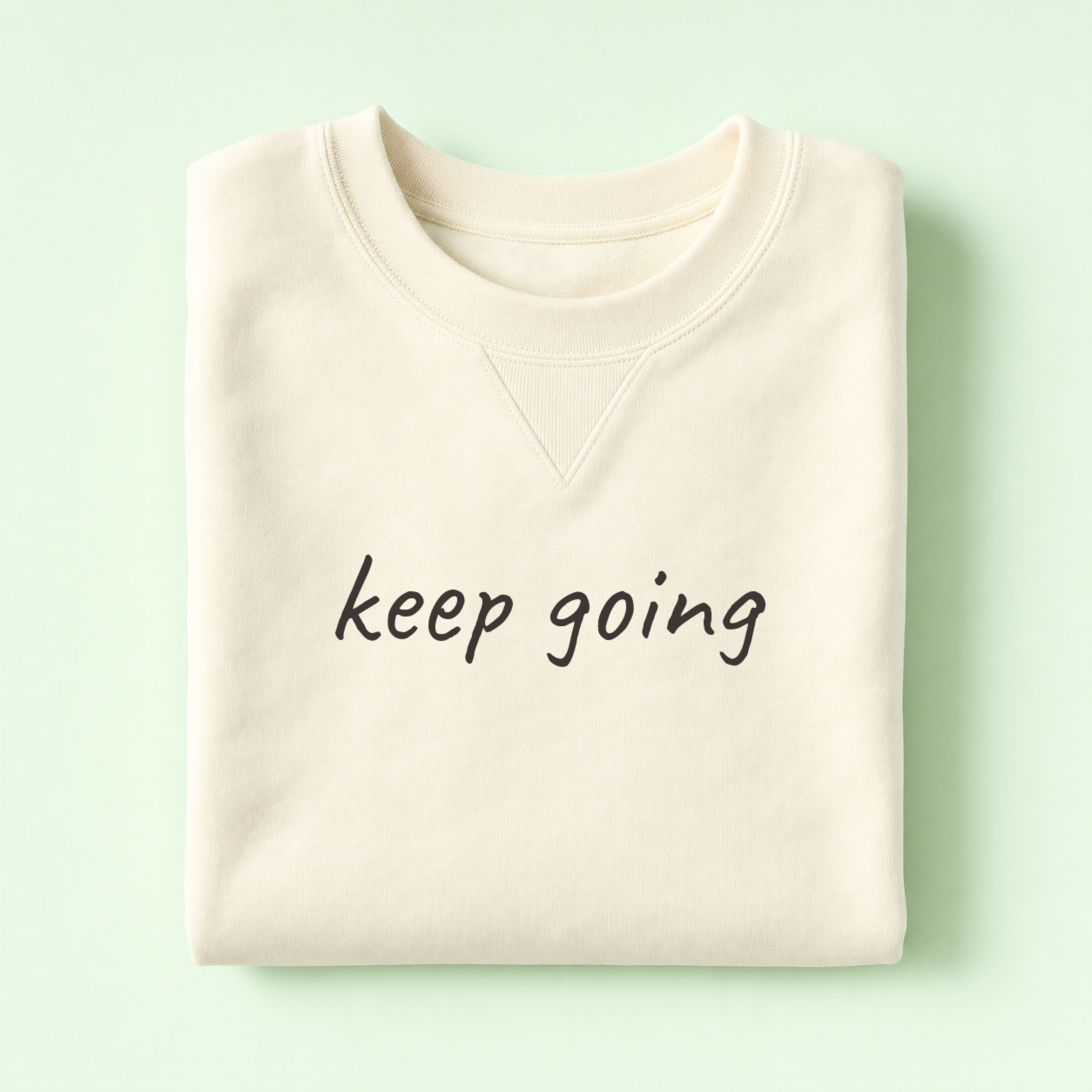 Folded ivory crewneck sweatshirt on a mint background