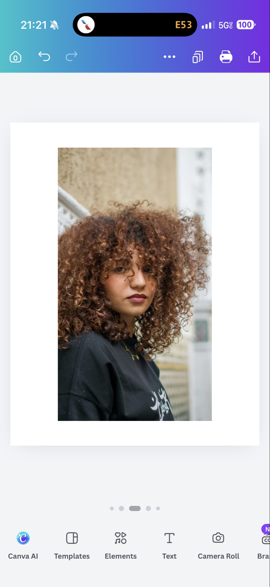 A woman with auburn curly hair wearing a black graphic tee and gold necklaces